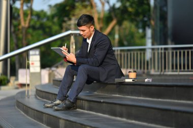 Sabahın erken saatlerinde iş merkezinin önündeki merdivenlerde dijital tablet kullanan iş adamı..