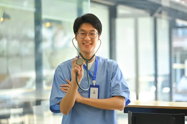 身穿蓝色制服的医生手持听诊器对着相机微笑的画像 保健和医疗概念 — 图库照片