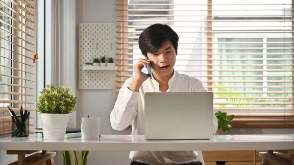 Yakışıklı Asyalı Serbest Çalışan Laptop Ekranına Bakıyor Cep Telefonuyla Konuşuyor — Stok fotoğraf