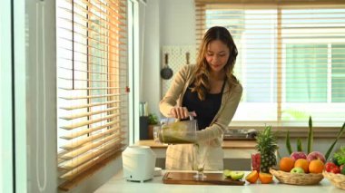 Genç bir kadın bardağa blenderla yeşil smoothie dolduruyor. Yüksek kalite 4k görüntü