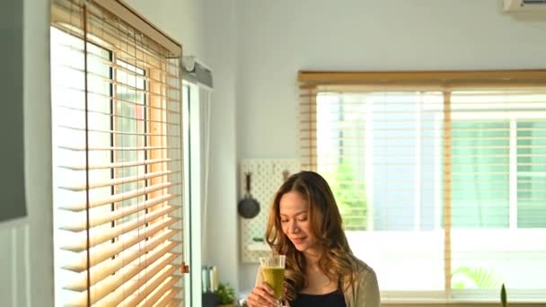 年轻的女人拿着一个绿色的冰沙在玻璃与搅拌机 水果和蔬菜在桌子上 高质量的4K镜头 — 图库视频影像