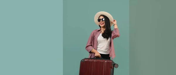 stock image Happy Asian woman wearing summer hat and sunglasses with luggage standing isolated turquoise blue green background.