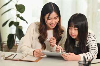 Anne, oturma odasında otururken uzaktan eğitim sırasında kızına ev ödevi için yardım ediyor..