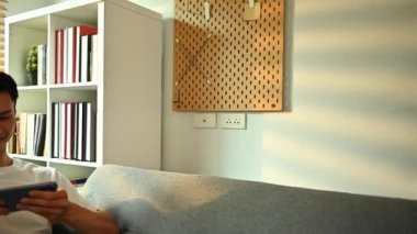 Kanepede dinlenirken video oyunu oynayan aşırı neşeli Asyalı adam. Teknoloji, eğlence ve eğlence aktivitesi..