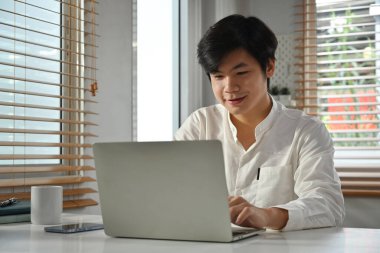 Akıllı günlük giyimli yakışıklı Asyalı girişimci dizüstü bilgisayardaki satış istatistik yönetimini analiz ediyor.