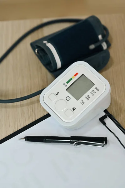 木製のテーブルの上に自動血圧モニターとクリップボード 高血圧 医療機器 — ストック写真