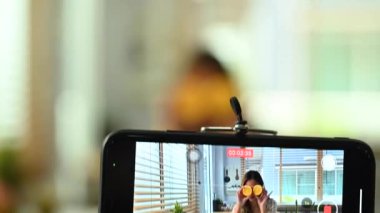 Portakal tutan kendine güvenen kadın beslenme uzmanı, çevrimiçi istişareler sunuyor veya akıllı telefondan video içeriği kaydediyor.