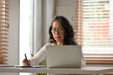 Gözlüklü, gülümseyen, dizüstü bilgisayarı olan ve kağıda not alan son sınıf öğrencisi. İnsanlar, teknoloji ve uzaktan çalışma konsepti.