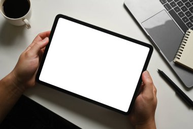 Adam çalışma masasında dijital tableti dizüstü bilgisayarın önünde tutuyor. Reklam metniniz için boş ekran.