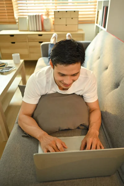 Расслабленный Азиатский Мужчина Лежит Диване Помощью Ноутбука Серфинг Интернет Работает — стоковое фото