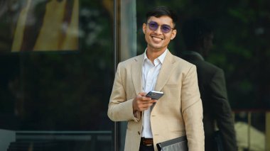 Milenyum işadamı ofis binasının önünde otururken akıllı telefon kullanıyor. Modern yaşam tarzı ve teknoloji kavramı.