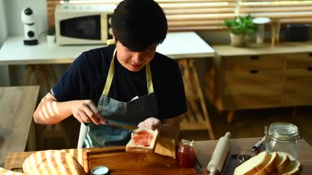 パンのスライスにジャムを広げるアジア人の男のショットを傾け 自宅で健康的な朝の食事を楽しむ — ストック動画