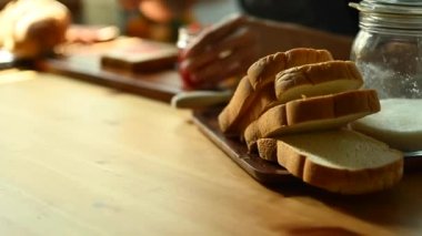 Adam sağlıklı bir kahvaltı hazırlıyor, bir dilim ekmeğe çilek reçeli sürüyor, mutfak masasında oturuyor..