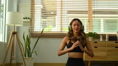 Kulaklıkla hoş müzik dinleyen ve oturma odasında yoga yapan çekici bir kadın. Spor ve sağlıklı yaşam tarzı..