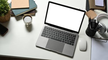 Bir dizüstü bilgisayar, kahve fincanı ve malzemeler beyaz ofis masasında. Reklam metniniz için boş ekran. 
