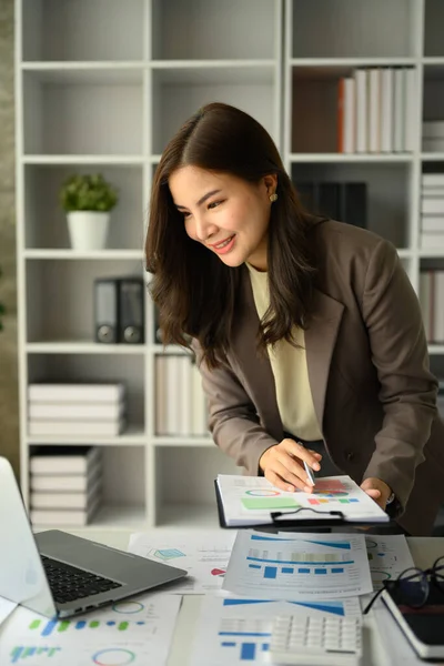 stock image Portrait of attractive young businesswoman standing at desk in modern office and using laptop computer.