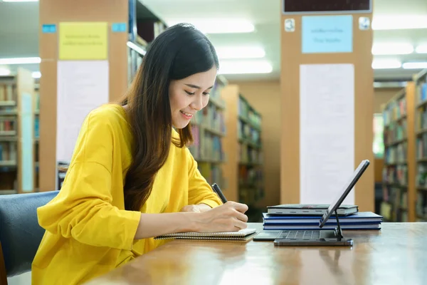 アジア系の学生の女性が課題を行い 図書館でデジタルタブレットを使用しています 技術の概念 — ストック写真