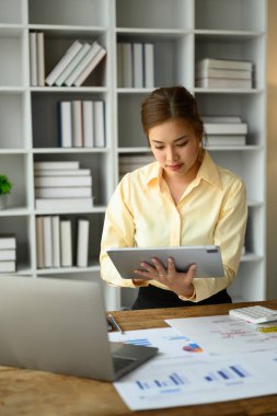 Dijital tablet üzerindeki finans piyasasını inceleyen konsantre kadın ekonomist çalışma masasında dururken....