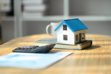 Gayrimenkul yatırımı ve kredisi, ipotek ve yeniden finanse konsepti. Ev modeli, hesap makinesi ve ahşap masa üzerindeki sözleşme..
