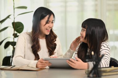 Genç Asyalı anne, küçük sevimli kızının evde uzaktan çalışmasına yardım ediyor..