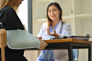 Omzunda askı olan yaralı bir kadın kemik uzmanıyla konuşuyor. Rehabilitasyon ve sağlık konsepti.