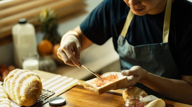 Genç adam kahvaltıda ya da mutfakta kahvaltıda ekmeğe ahududu reçeli sürüyor..