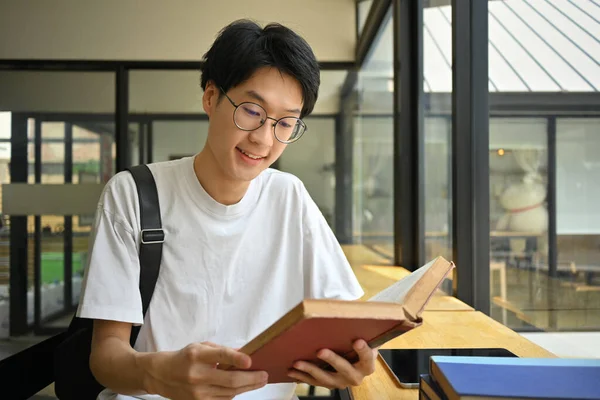 喫茶店に座って本を読んでいるメガネ姿のアジア系男性学生を笑顔にする 技術の概念 — ストック写真