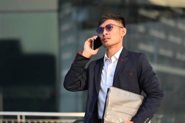 Şehirdeki modern ofis binasının yanında duran ve cep telefonuyla konuşan yakışıklı başarılı iş adamı..