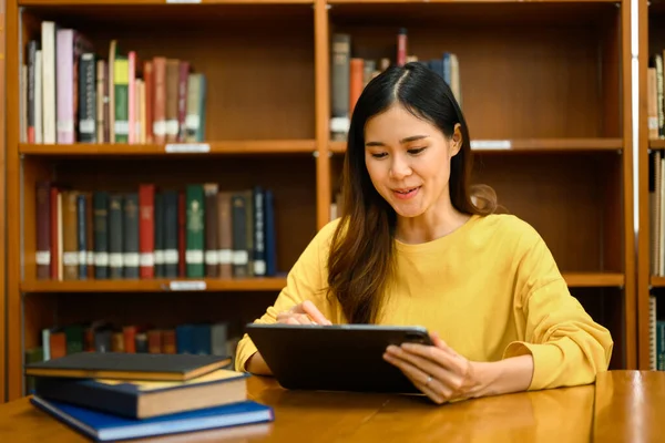 図書館でオンライン情報を検索するためにデジタルタブレットを使用してアジアの女性学生に焦点を当てました 教育と技術の概念 — ストック写真