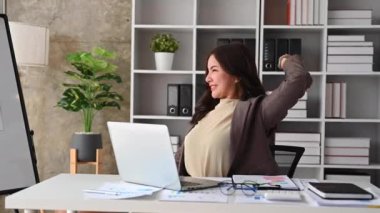 Happy relaxed millennial businesswoman stretching her arms above her head at comfortable office chair.