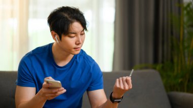 Günlük giysiler içinde kredi kartı tutan ve iinternet ya da internet üzerinden ödeme yapmak için akıllı telefon kullanan bir adam..