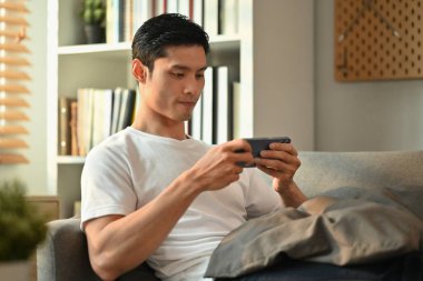 Evde akıllı telefondan video oyunu oynayan konsantre bir adam. Teknoloji, eğlence ve eğlence aktivitesi.