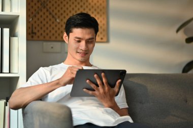 Kanepede oturup dijital tablet kullanan yakışıklı bir serbest yazar. İletişim, insanlar, teknoloji kavramı.