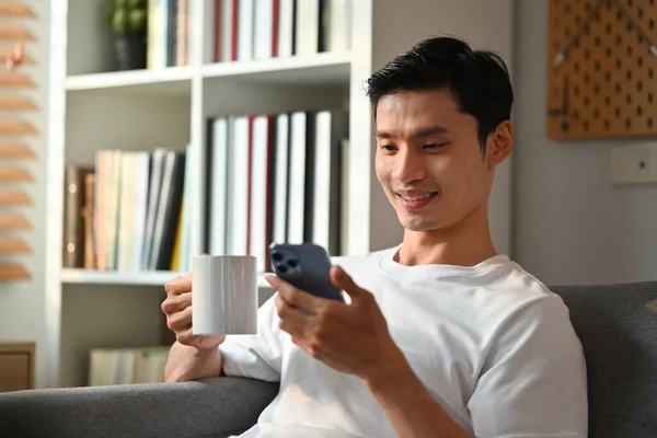 매력적 남자가 거실에서 소파에서 쉬면서 커피를 마시고 전화로 — 스톡 사진
