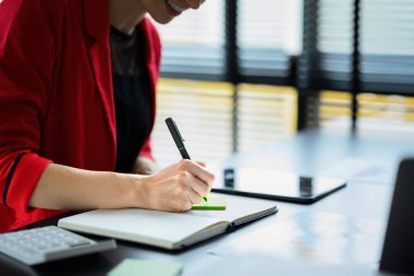 Önemli notlar alan, günlük randevu planlayan ve iş seyahatini günlüğüne yazan kadın işçinin kırpılmış görüntüsü..