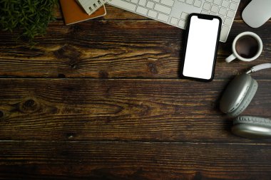 Akıllı telefonun boş ekranı, kulaklığı, kahve fincanı ve klavyesi ahşap çalışma masasında. Metin için alanı kopyala.
