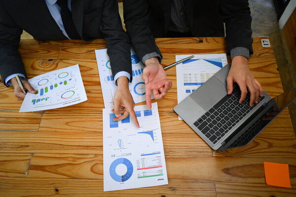 Overhead view of businesspeople analyzing financial data, stock market information at meeting table.
