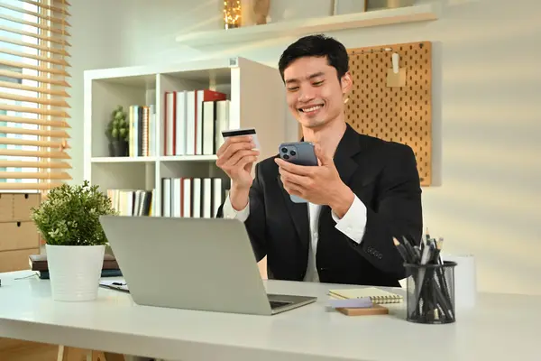 Nöjd Asiatisk Manlig Arbetstagare Som Innehar Kreditkort Och Använder Smartphone — Stockfoto