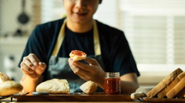 Mutlu adam kahvaltı hazırlıyor ve ekmek dilimine ahududu reçeli yayıyor..