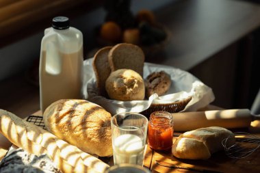 Mutfaktaki ahşap masada pişmiş ekmek ve bir bardak süt. Pencereden gelen güneş ışığıyla birlikte. Sağlıklı beslenme ve geleneksel fırın konsepti.