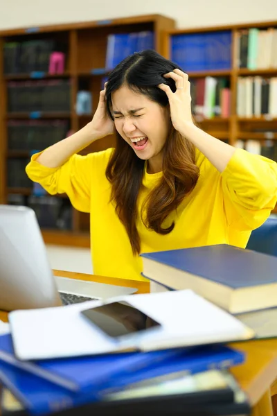 Stressed female student sitting in front of the laptop, having serious computer problem or feeling tired of studying for college exam.