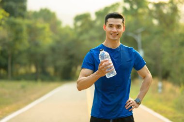 Spor şişesini suyla tutan genç bir fitness oyuncusunun görüntüsü. Açık hava seansında mola veriyor..