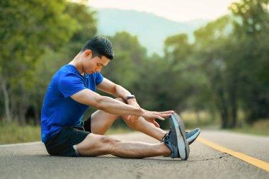 Spor giyimli kaslı atletik adam antrenmandan sonra dinleniyor ve bacaklarını esnetiyor. Fitness, eğitim ve sağlıklı yaşam tarzı.