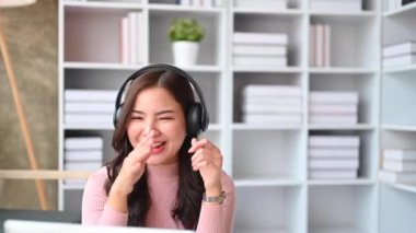 Kulaklıkla el sallayan neşeli genç bir kadın, dizüstü bilgisayardan video görüşmesi yapıyor. İnsanlar, teknoloji ve iletişim..