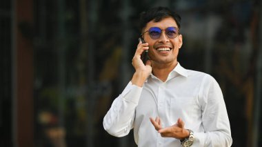 Bin yıllık resmi giyimli çekici iş adamı dışarıda cep telefonuyla konuşuyor. İş, teknoloji ve yaşam tarzı.