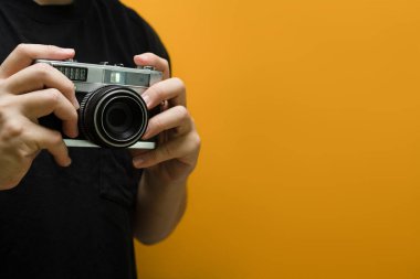 Sarı zemin üzerinde fotokopi alanı olan retro fotoğraf makinesini tutan adam elleri.
