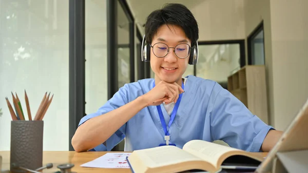 ヘッドフォン読書本のアジアの男性医療学生 図書館での大学試験の準備 医療インターンシップの概念 — ストック写真