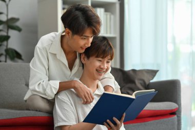 Mutlu eşcinsel çift evdeki kanepede kitap okuyor, hafta sonları birlikte vakit geçiriyorlar. LGBTQ insanları yaşam tarzı ve duyguları seviyor.