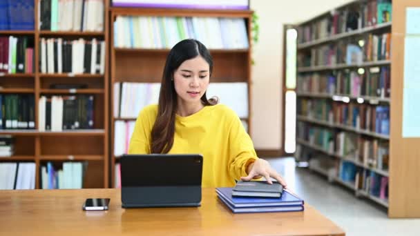 魅力的なアジアの女性学生の本を開き スタートアッププロジェクトのためのデジタルタブレットを使用して 情報をオンラインで研究 — ストック動画
