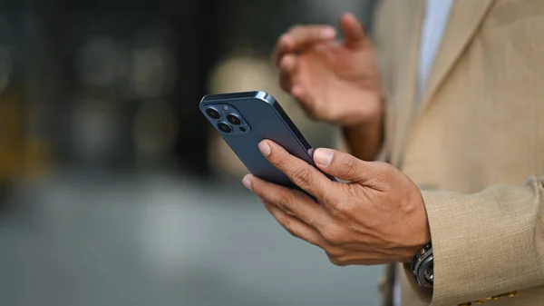 stock image Select focus on hand of businessman using smartphone while standing outdoor. Technology, business and communicating.